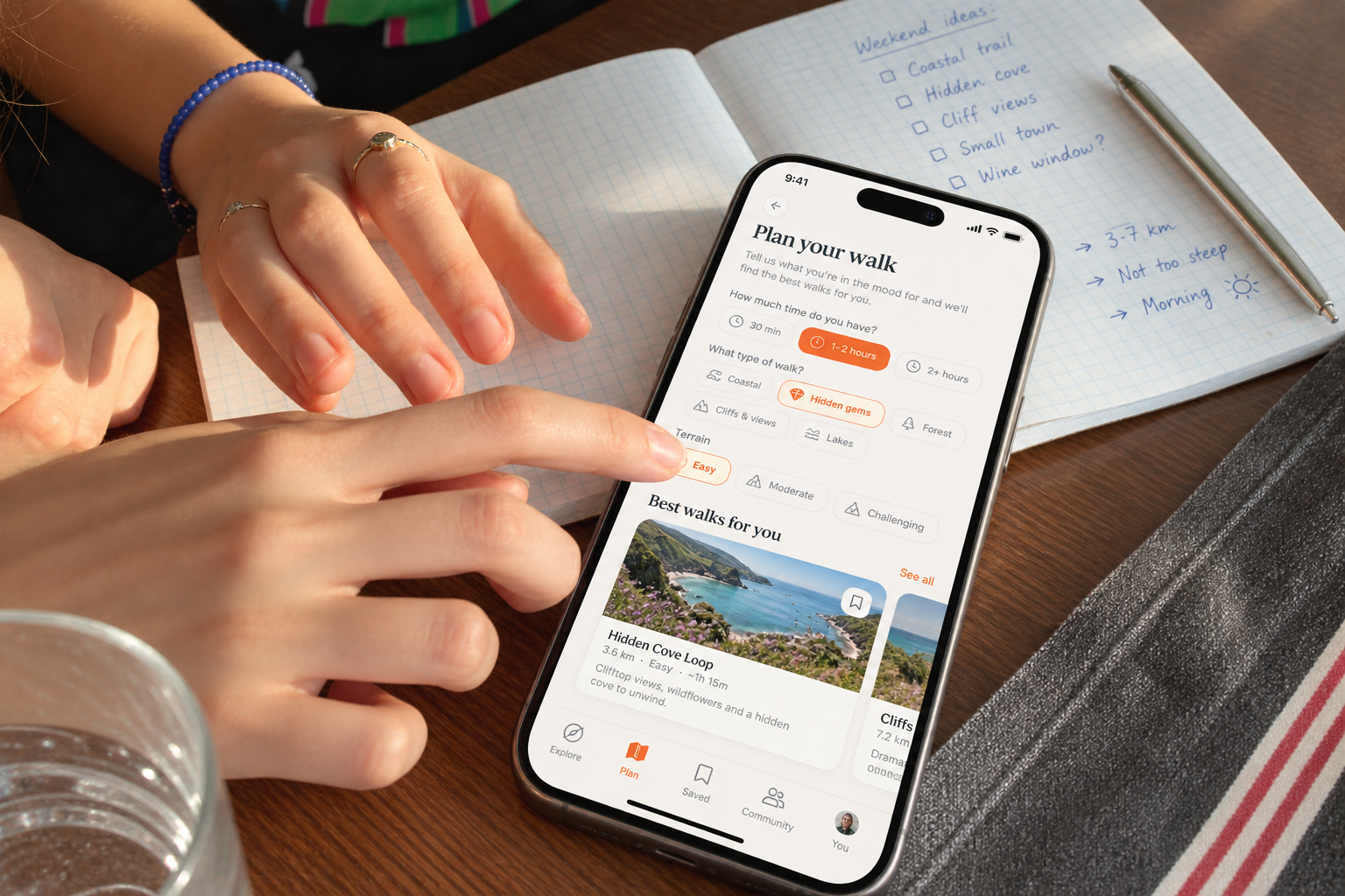 Hands planning a walk beside a notebook, with a RoveWalk phone screen showing time and mood filters plus a recommended coastal walk.