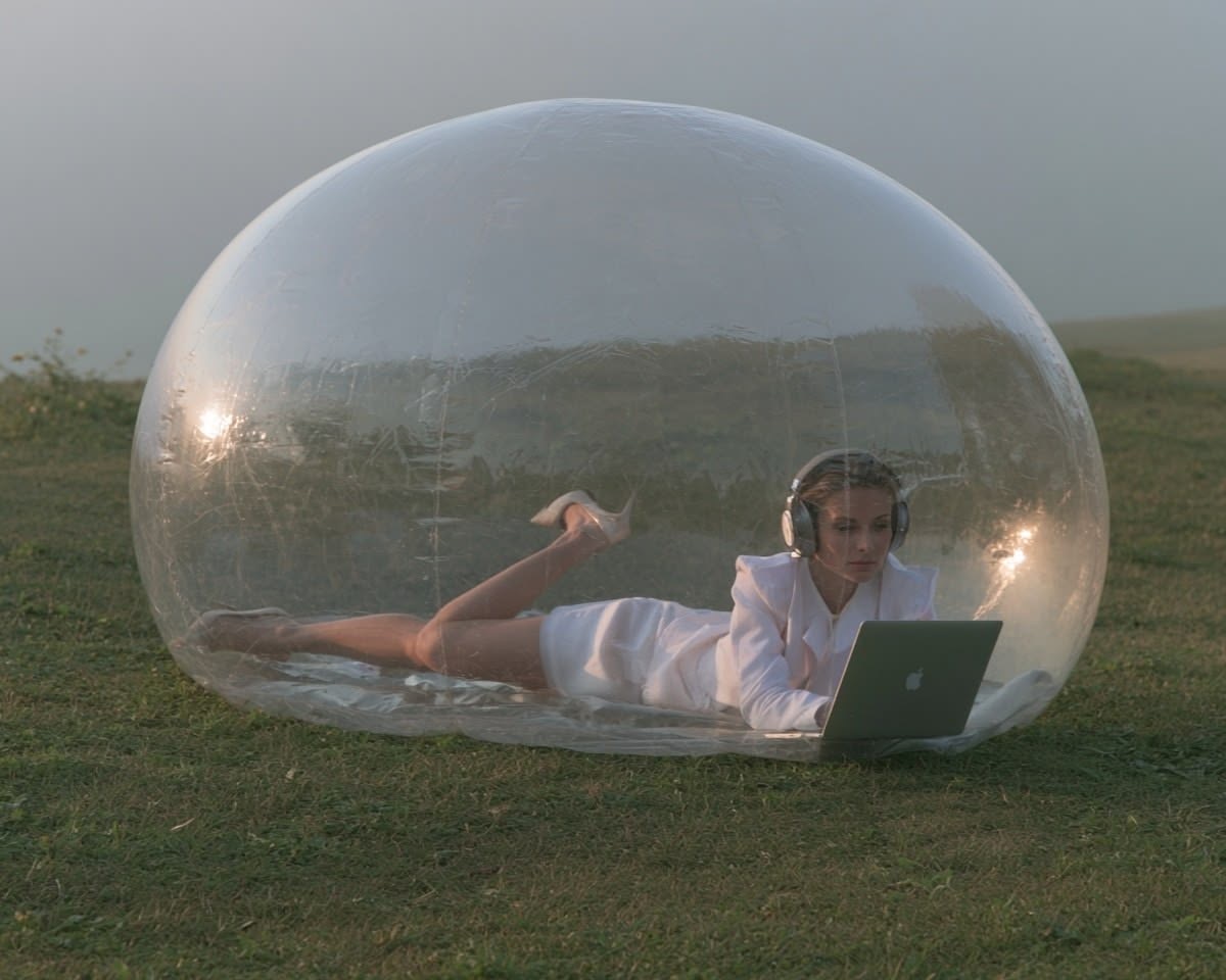 Woman using a laptop inside a transparent bubble outdoors